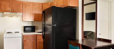 Une cuisine avec des meubles de rangement en bois, un réfrigérateur noir, une cuisinière blanche et un four à micro-ondes.