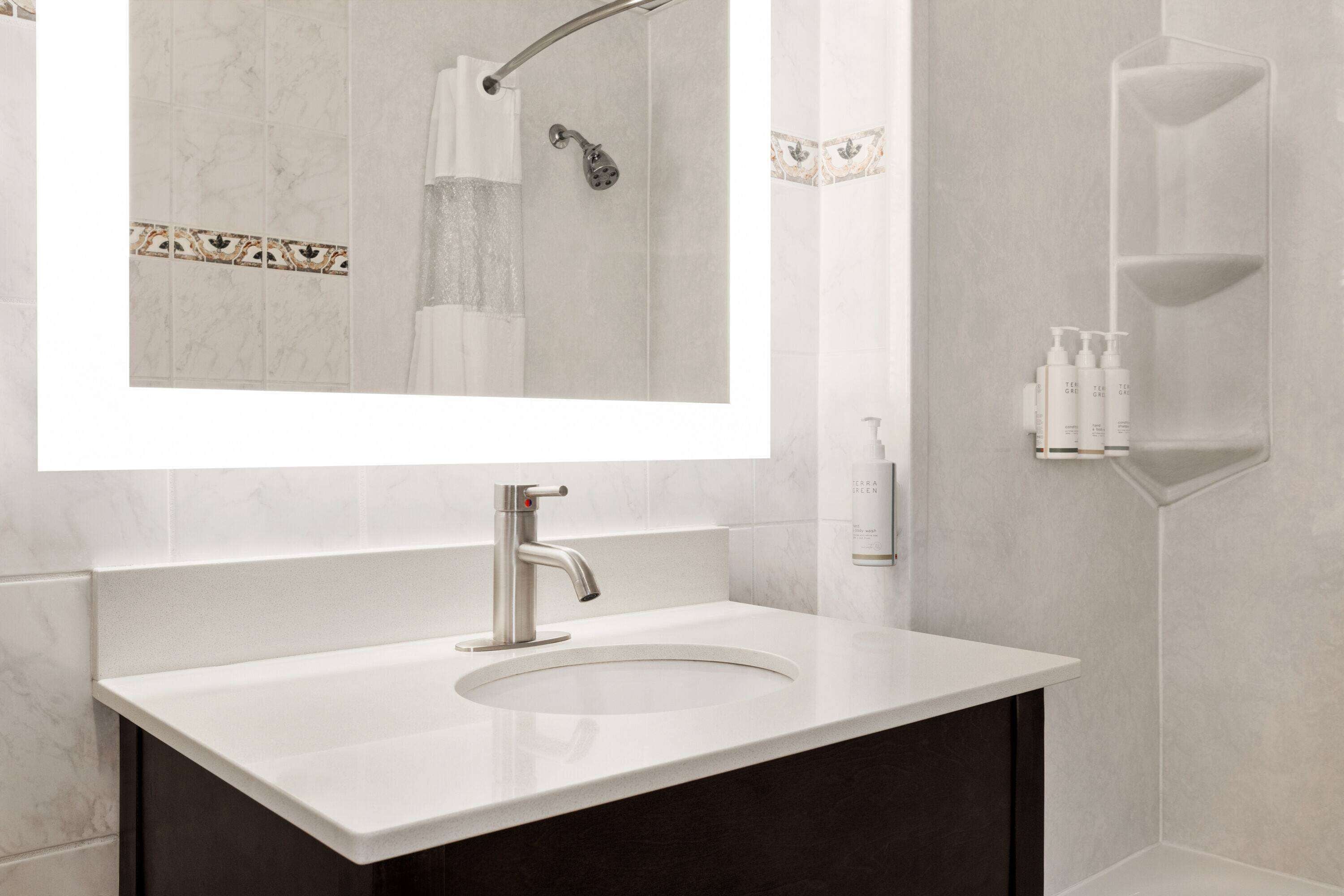 A modern bathroom with a white sink, a large mirror, and a shower area.