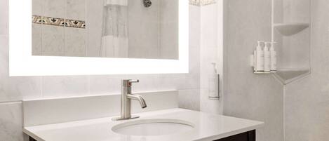 Un baño moderno con un lavamanos blanco, un espejo grande y una zona de ducha.