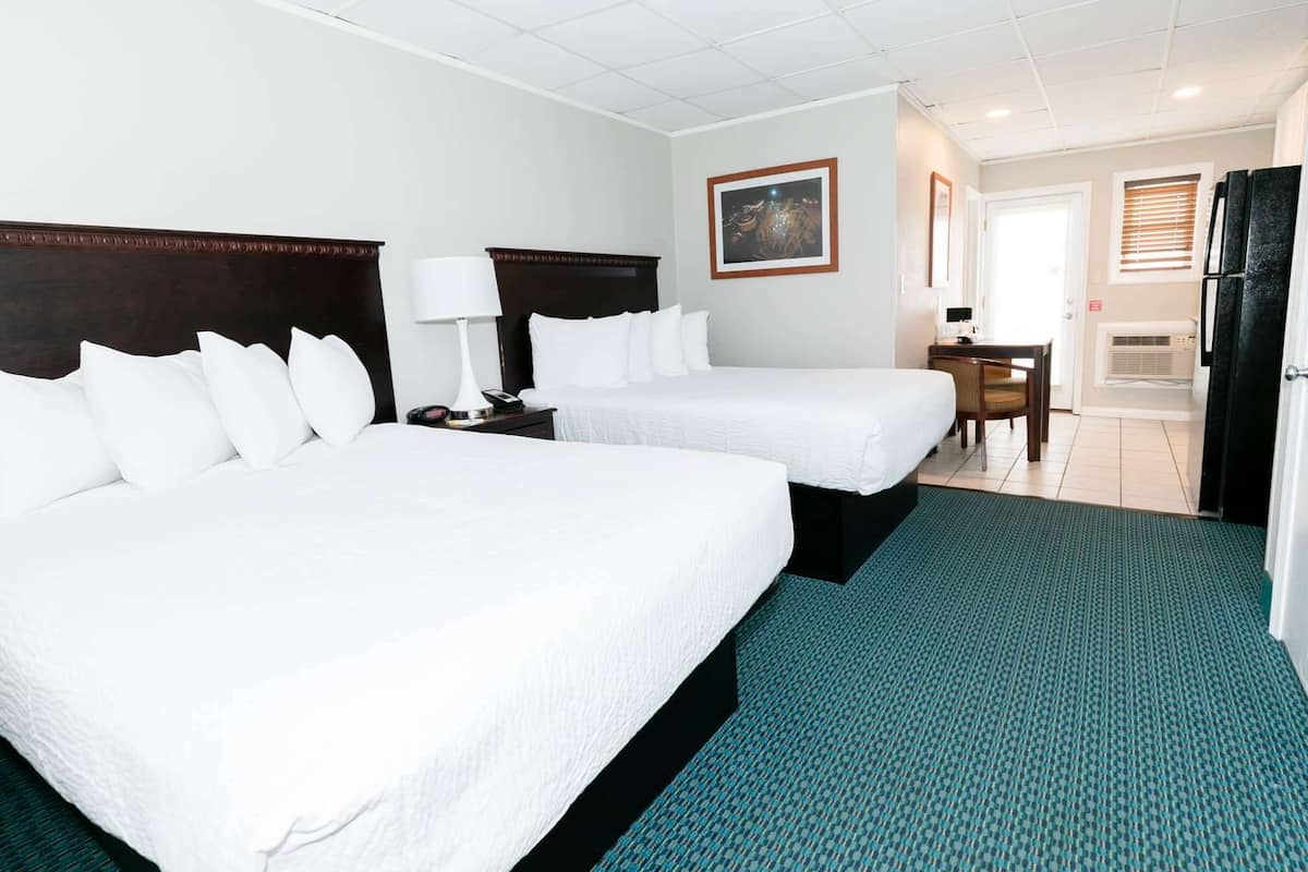A hotel room with two beds, a desk, a chair, a refrigerator, and a painting on the wall.