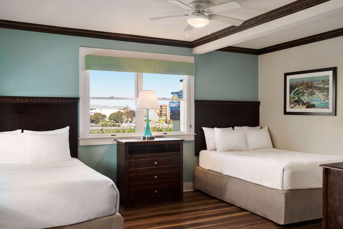 A hotel room with two beds, a dresser, a window with a view, and a ceiling fan.