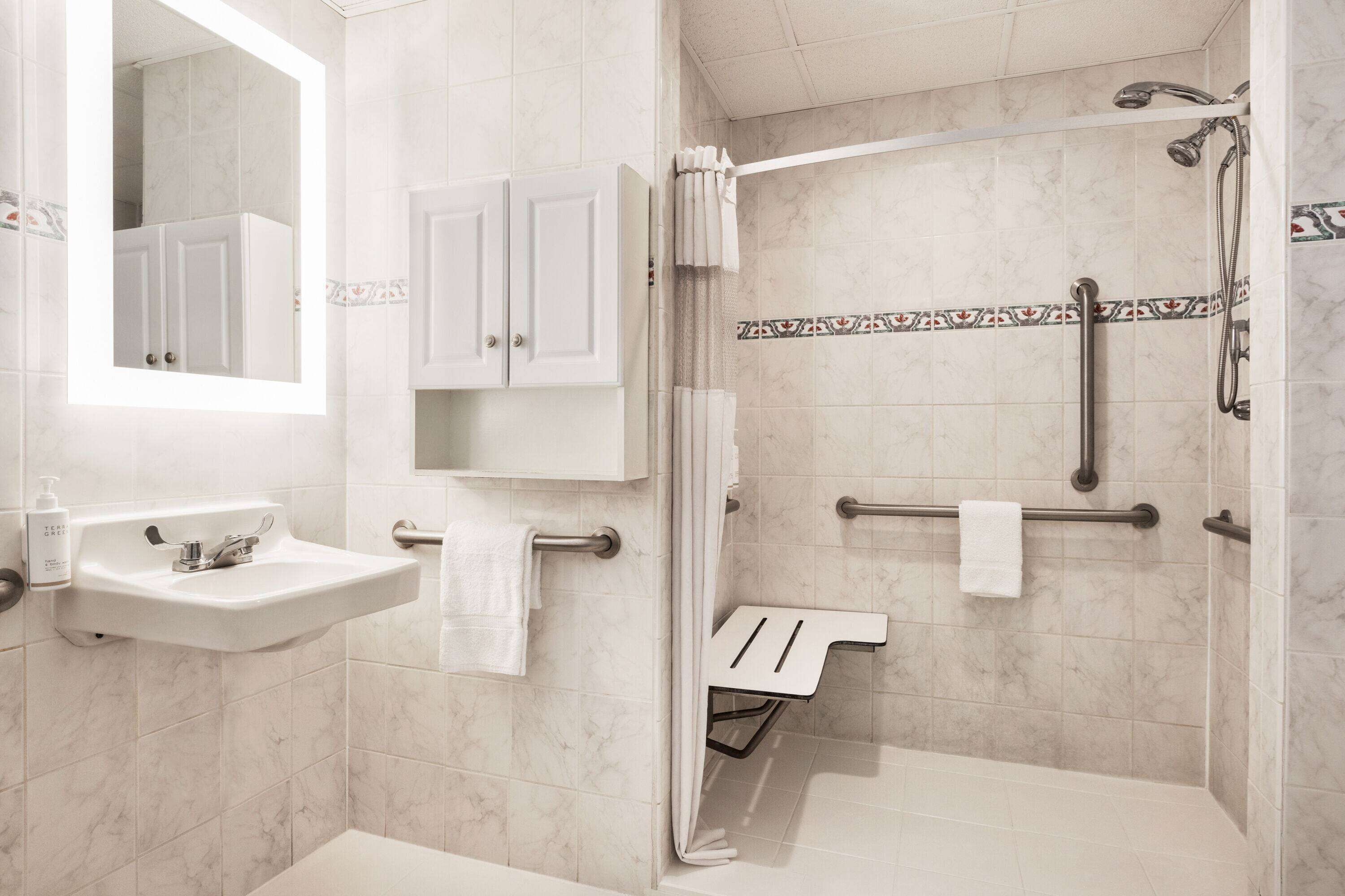 A modern bathroom with a sink, mirror, cabinets, shower, and grab bars.