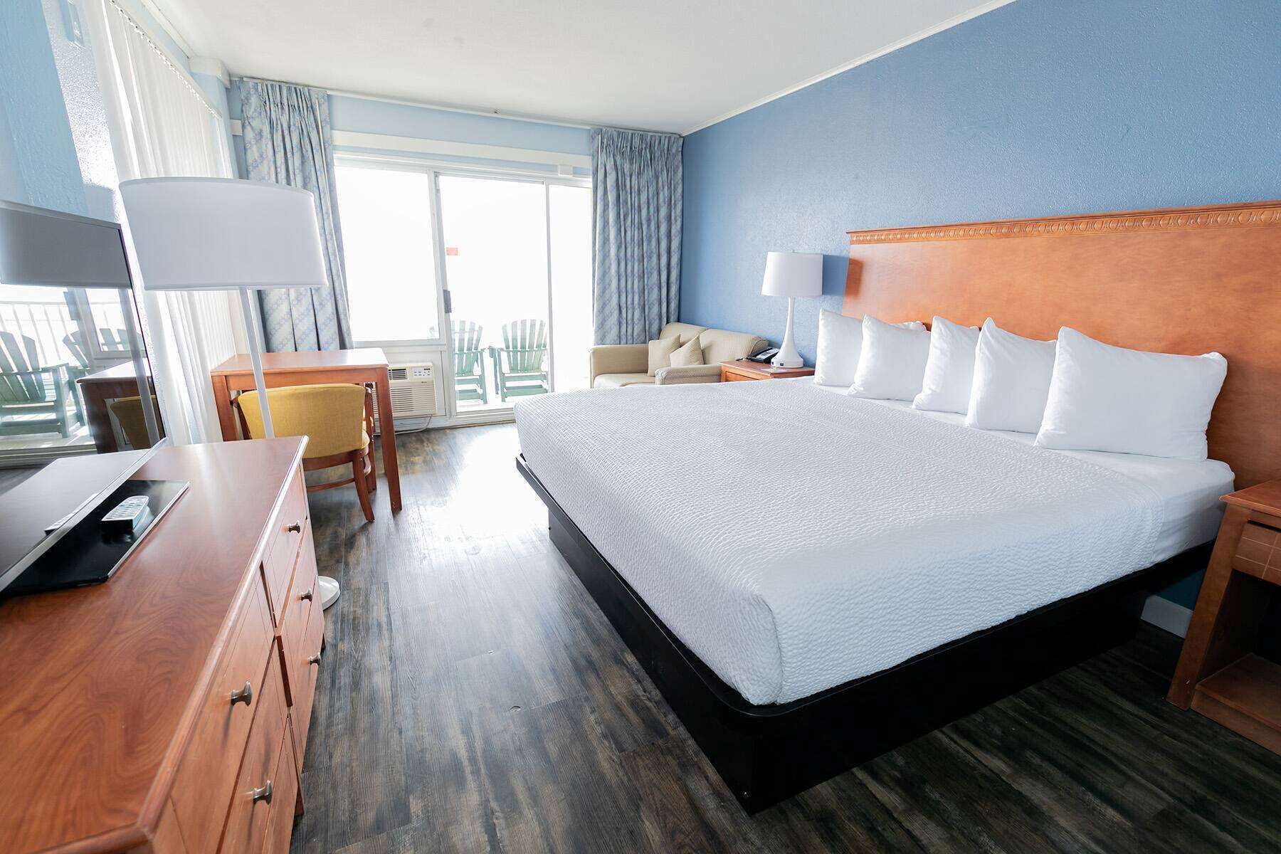 Een hotelkamer met een groot bed, een bureau met een computer, een stoel en uitzicht naar buiten door een raam.