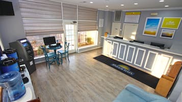 A hotel lobby with a reception desk, a seating area with chairs, a water dispenser, and a large window with blinds.