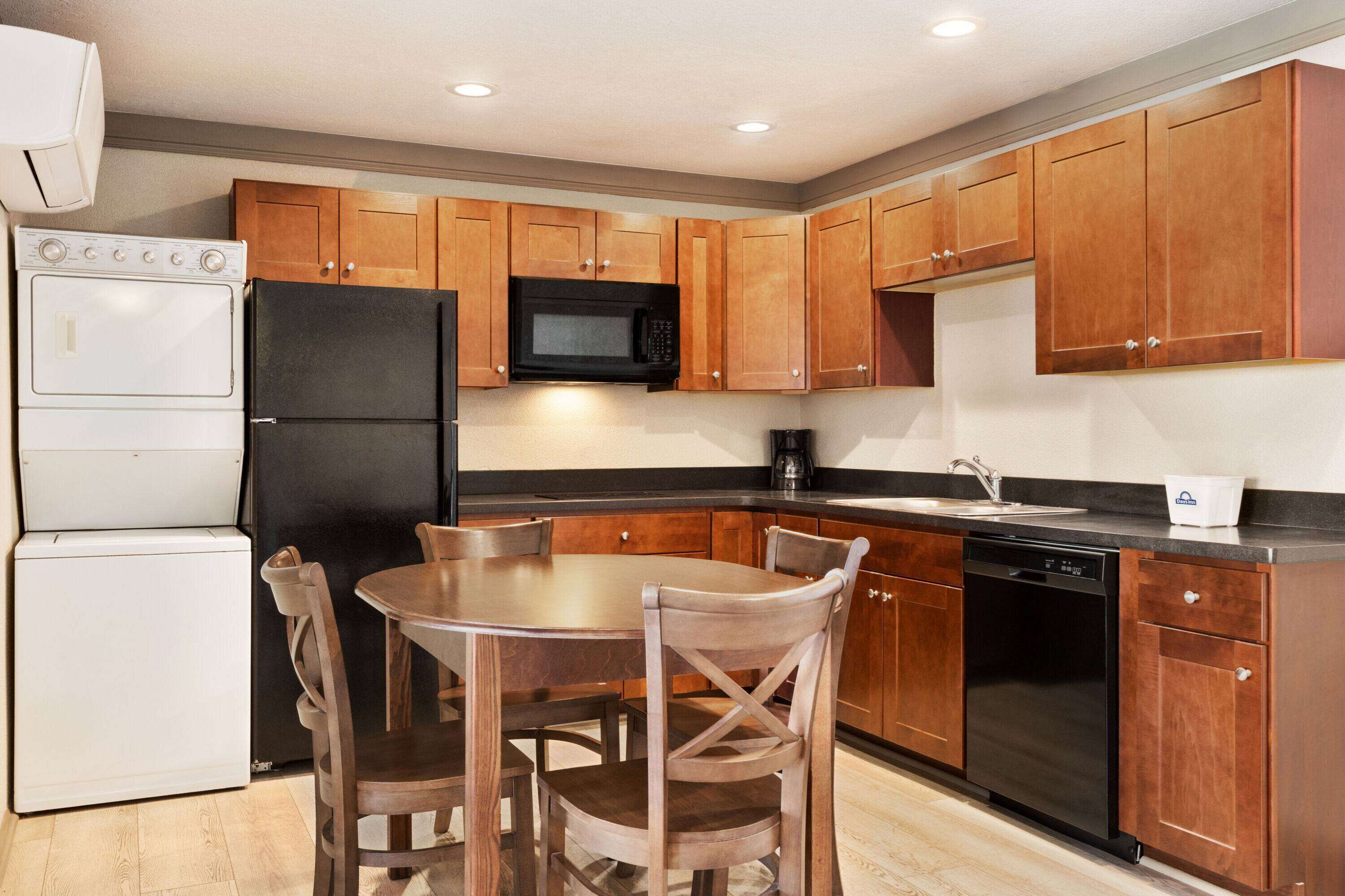 A compact kitchen with wooden cabinets, a black refrigerator, a microwave, a dishwasher, and a sink.