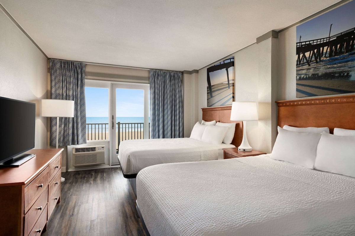 A hotel room with two beds, a TV, a dresser, and a view of the ocean.