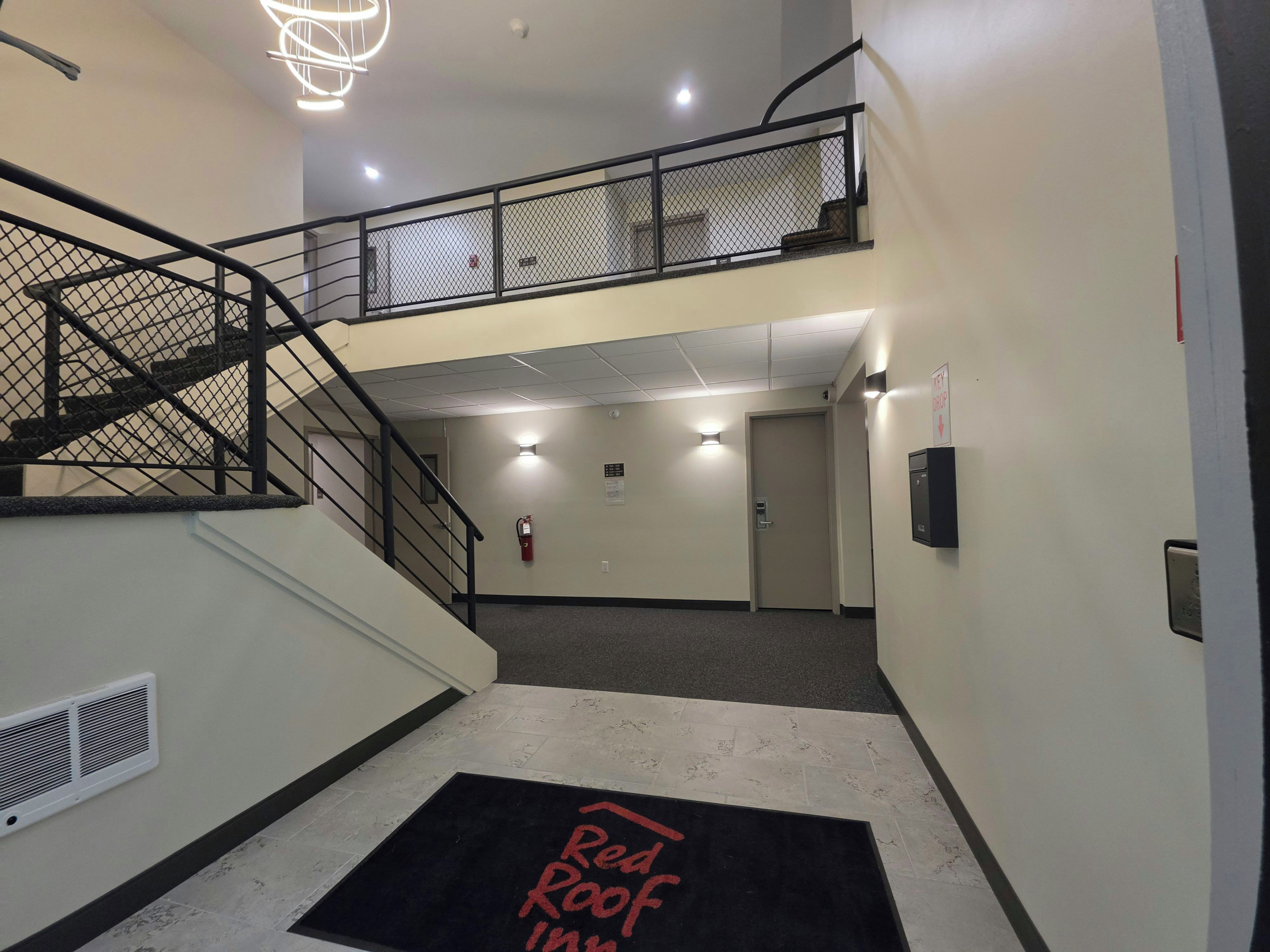 A hotel interior with a staircase, a fire extinguisher, a door, and a Red Roof Inn sign on the floor.