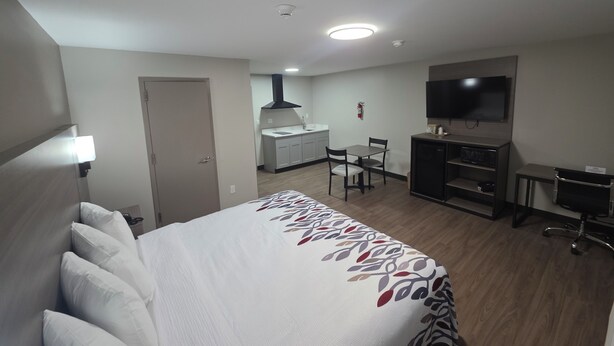 Una habitación de hotel con cama, escritorio, silla, televisión y kitchenette.
