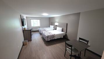 Ein Hotelzimmer mit Bett, Nachttisch, Schreibtisch, Stuhl und einem Fenster.