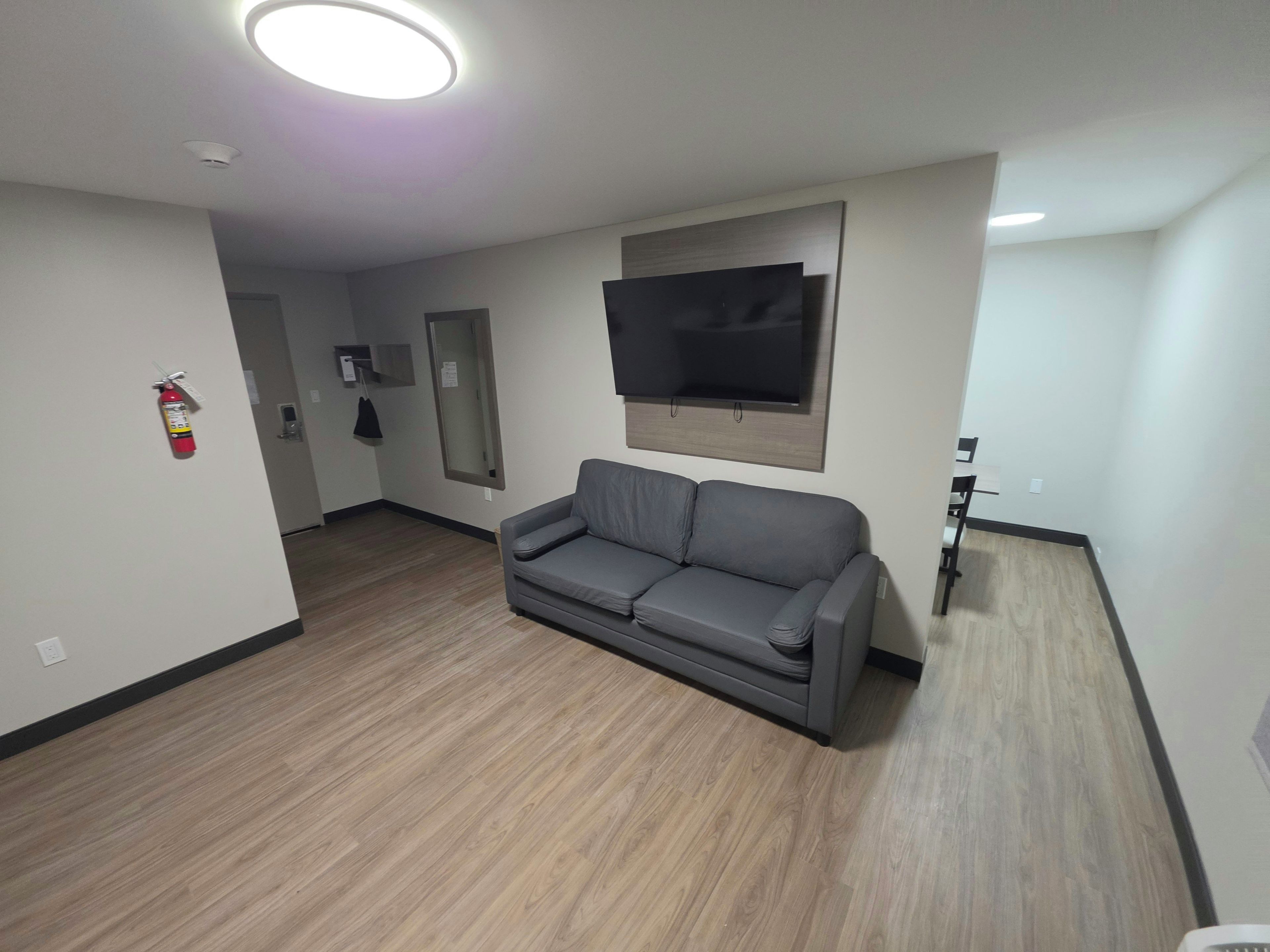 A modern living room with a grey sofa, a mounted TV, and a fire extinguisher on the wall.