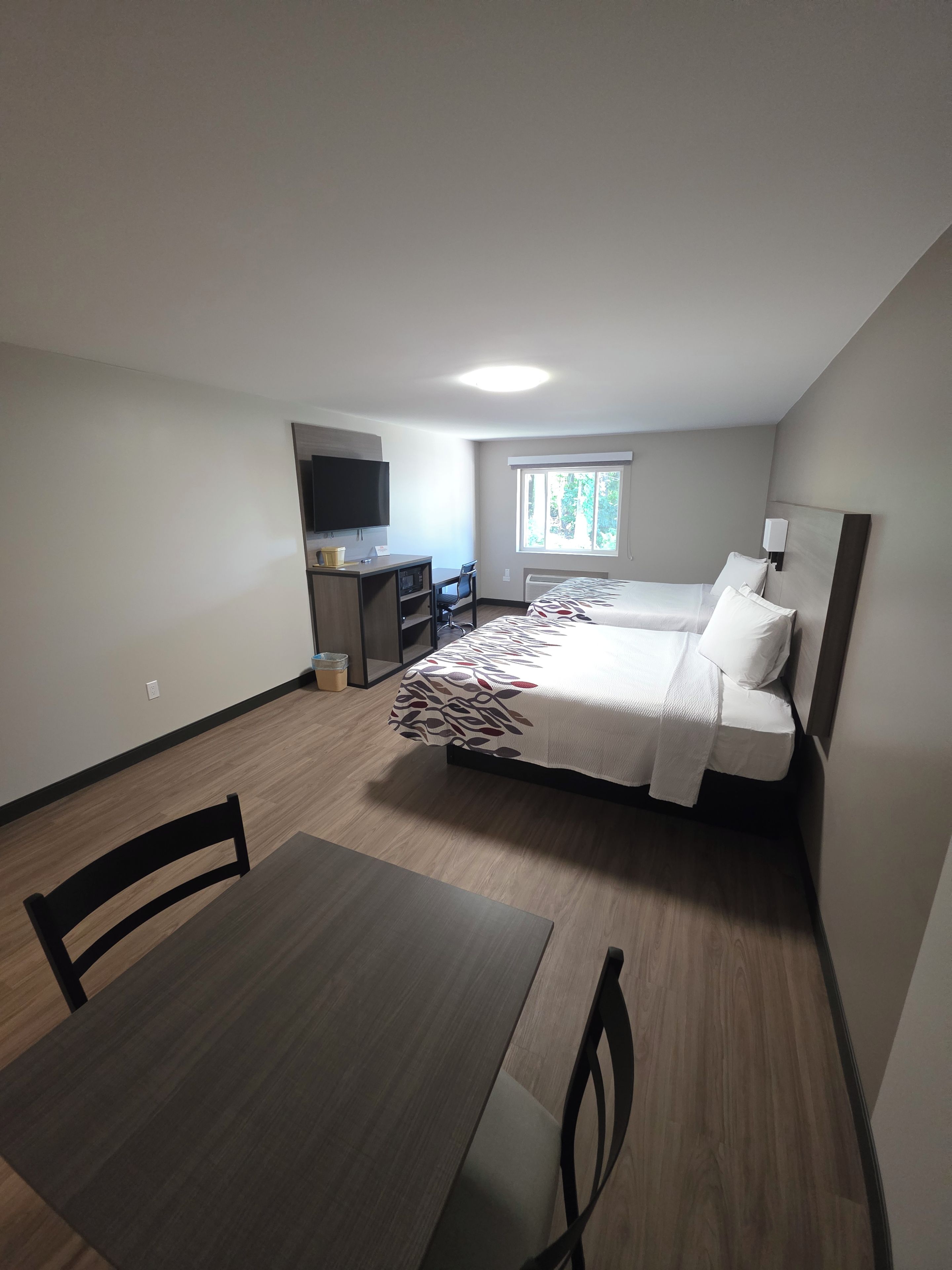 A compact hotel room with a bed, a desk, a chair, a television, and a window.