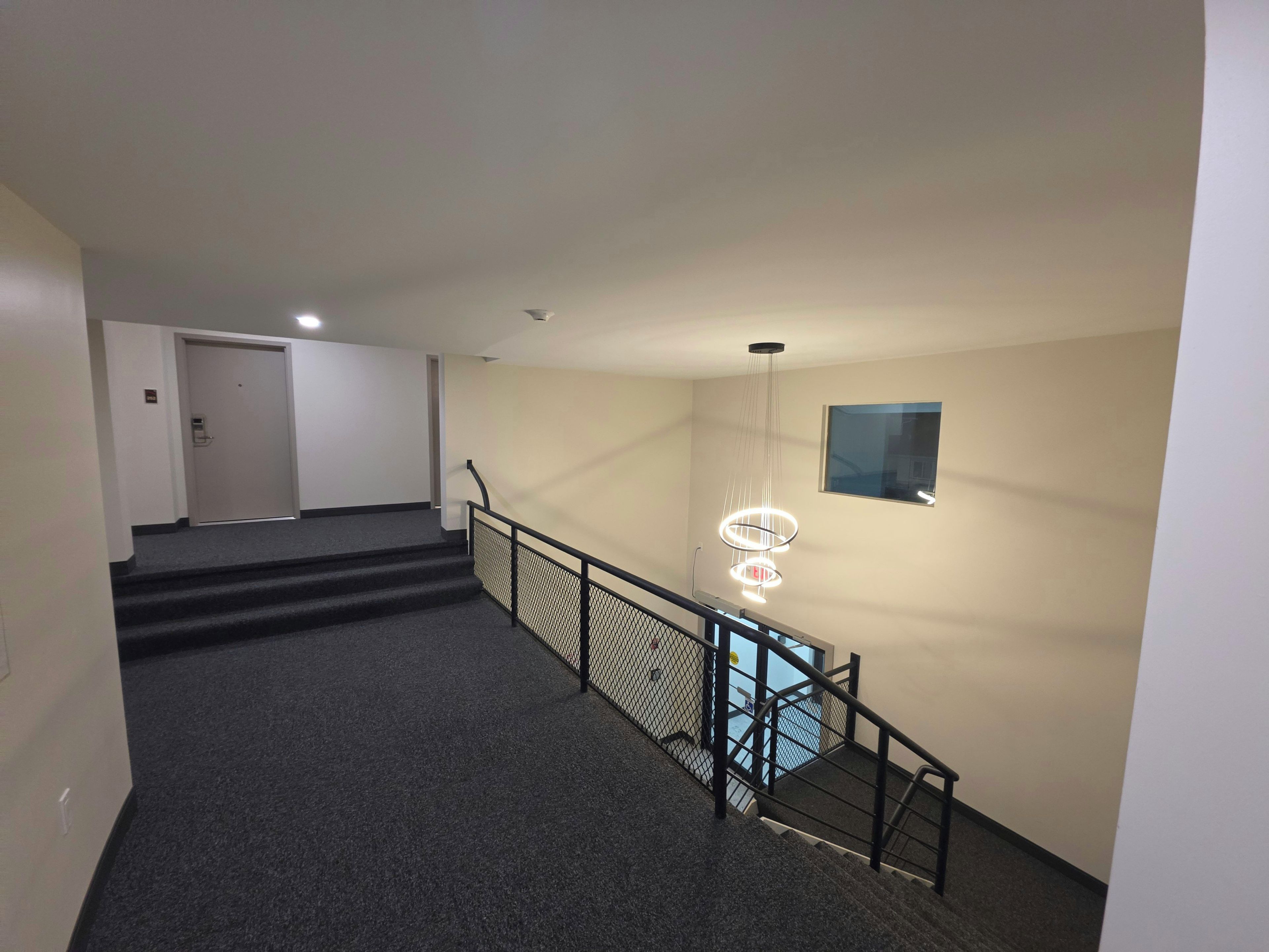 A staircase with a handrail, carpeted steps, and a modern light fixture.
