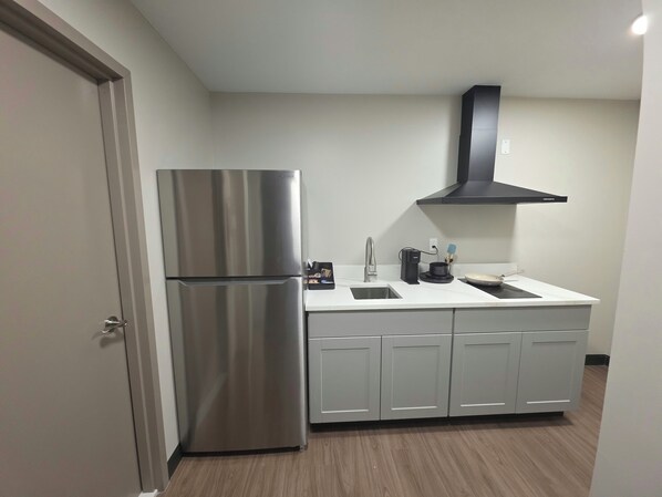 Una cocina compacta con refrigerador de acero inoxidable, campana extractora negra y encimera blanca.
