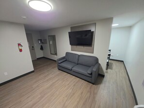A living room with a grey sofa, a mounted TV, and a fire extinguisher on the wall. - Red Roof Inn Sutton (Sutton)