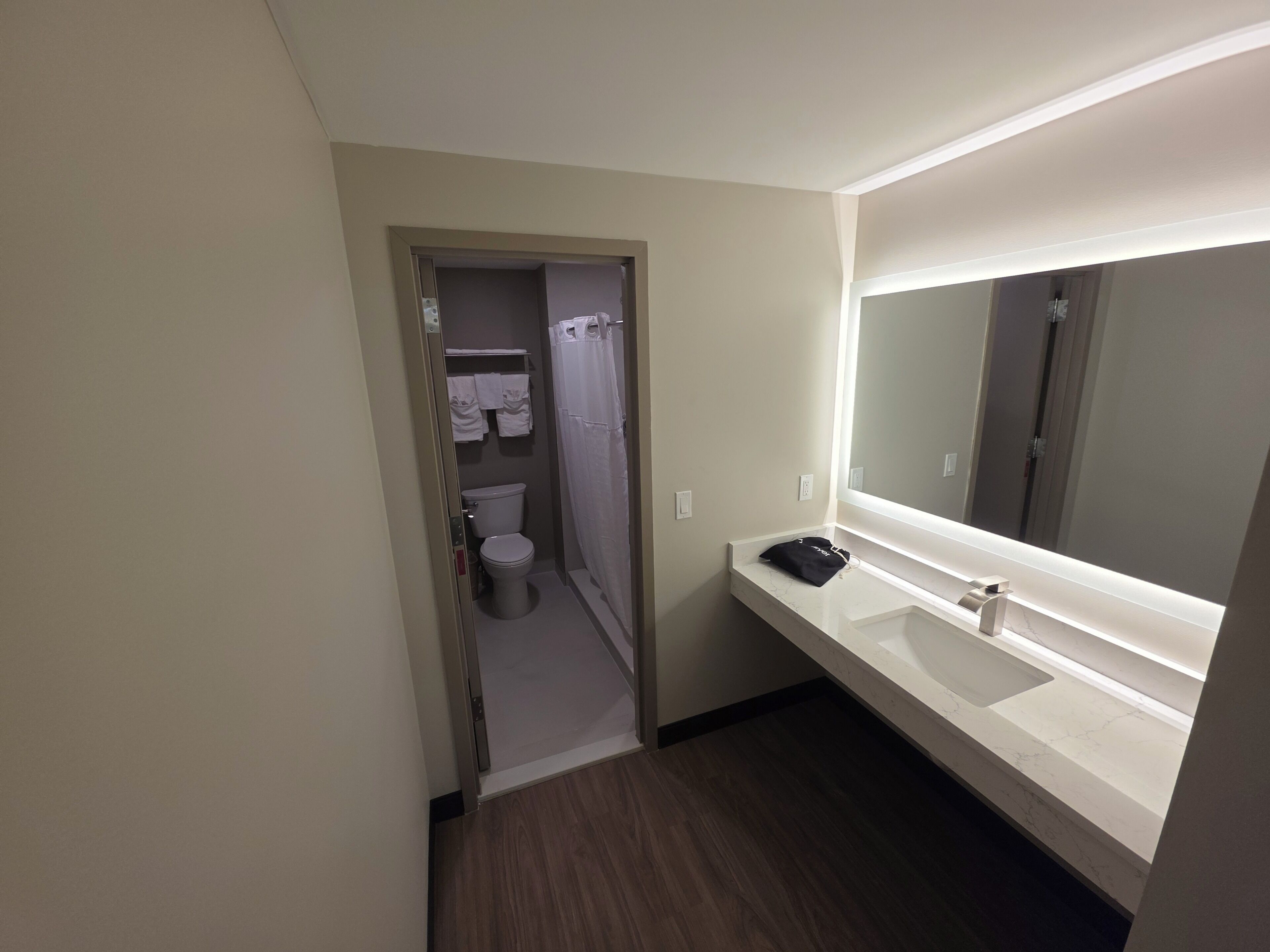 A hotel bathroom with a toilet, a sink, a mirror, and a shower curtain.