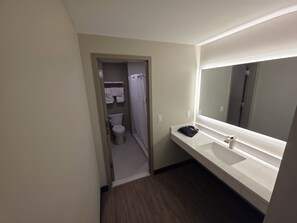 A hotel bathroom with a toilet, a sink, a mirror, and a shower curtain.