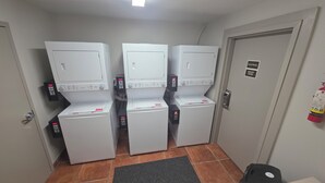 Un lavadero con tres lavadoras apiladas, un extintor y una puerta con letrero de cuarto eléctrico y de calderas.