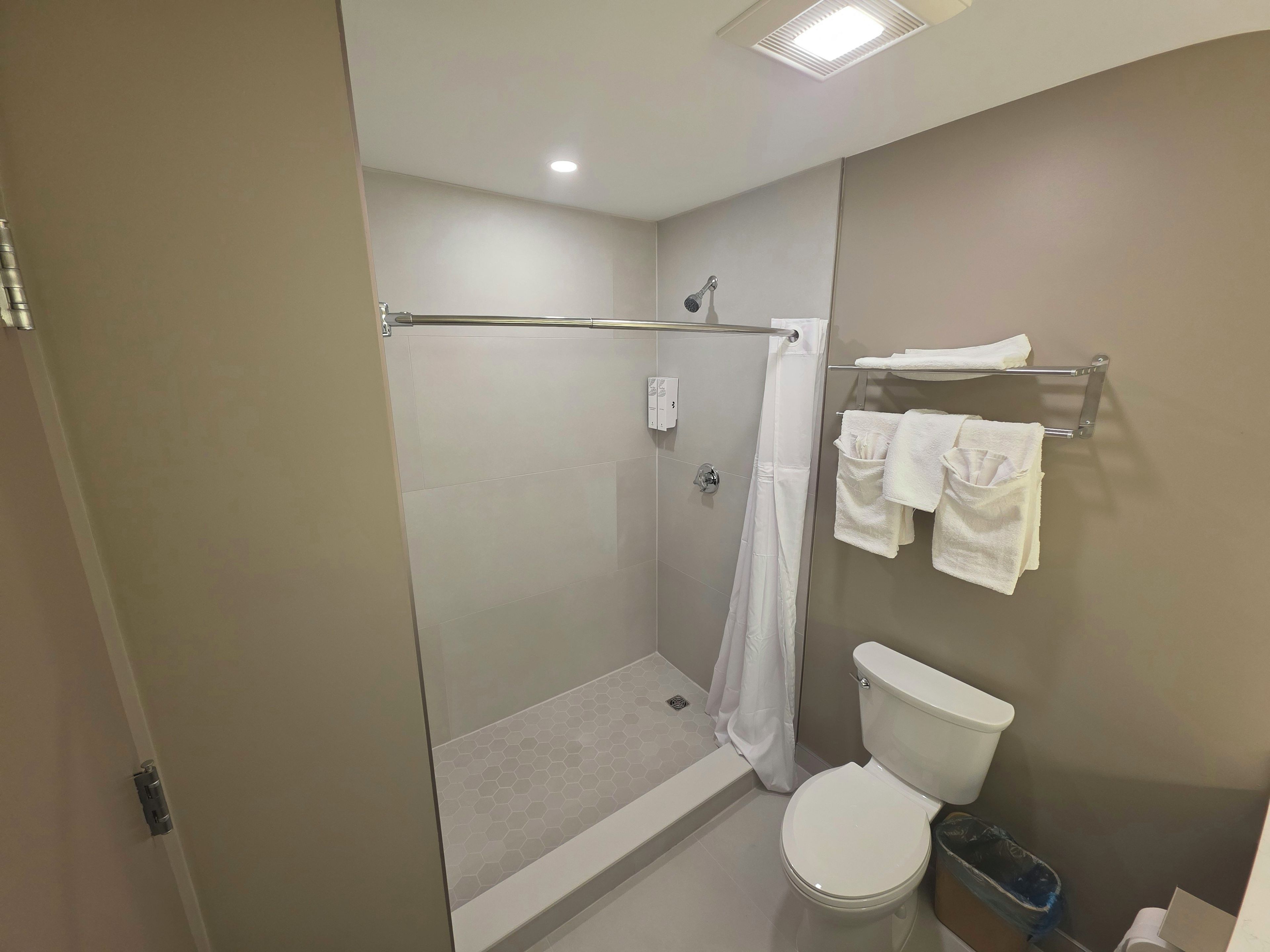 A bathroom with a glass-enclosed shower, a toilet, and a towel rack with towels.