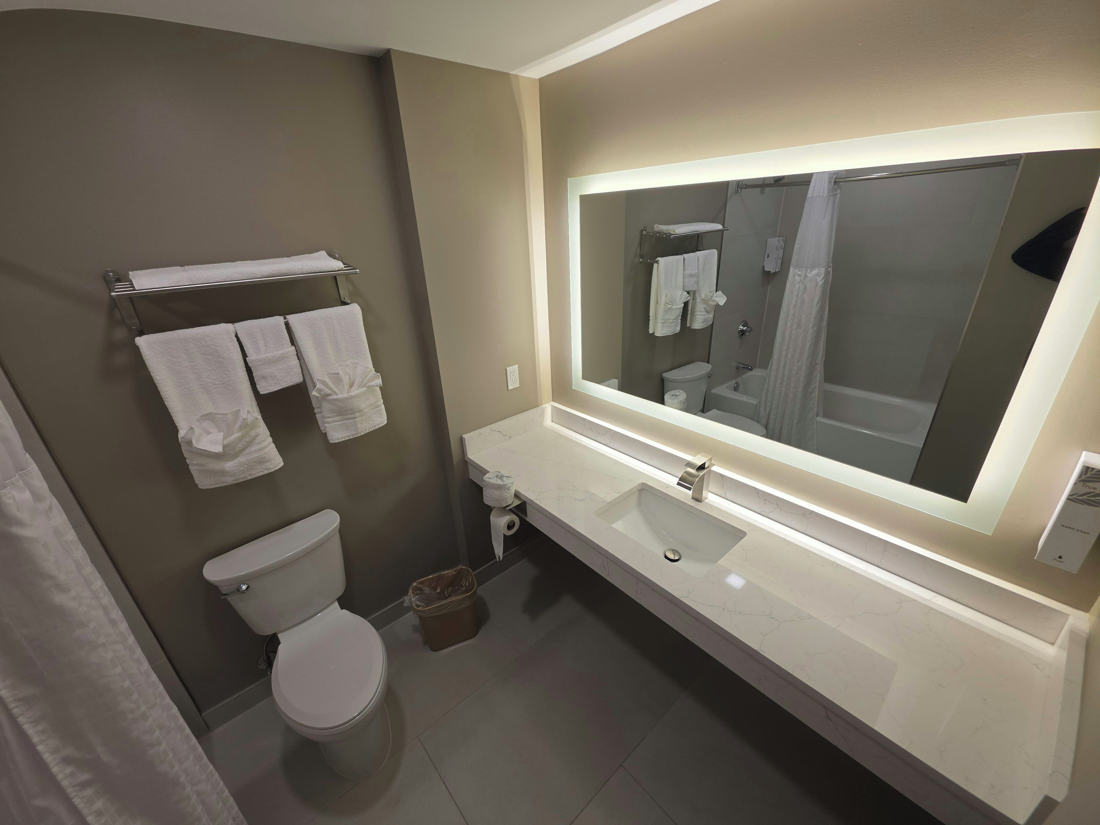 A modern bathroom with a toilet, sink, and large mirror.