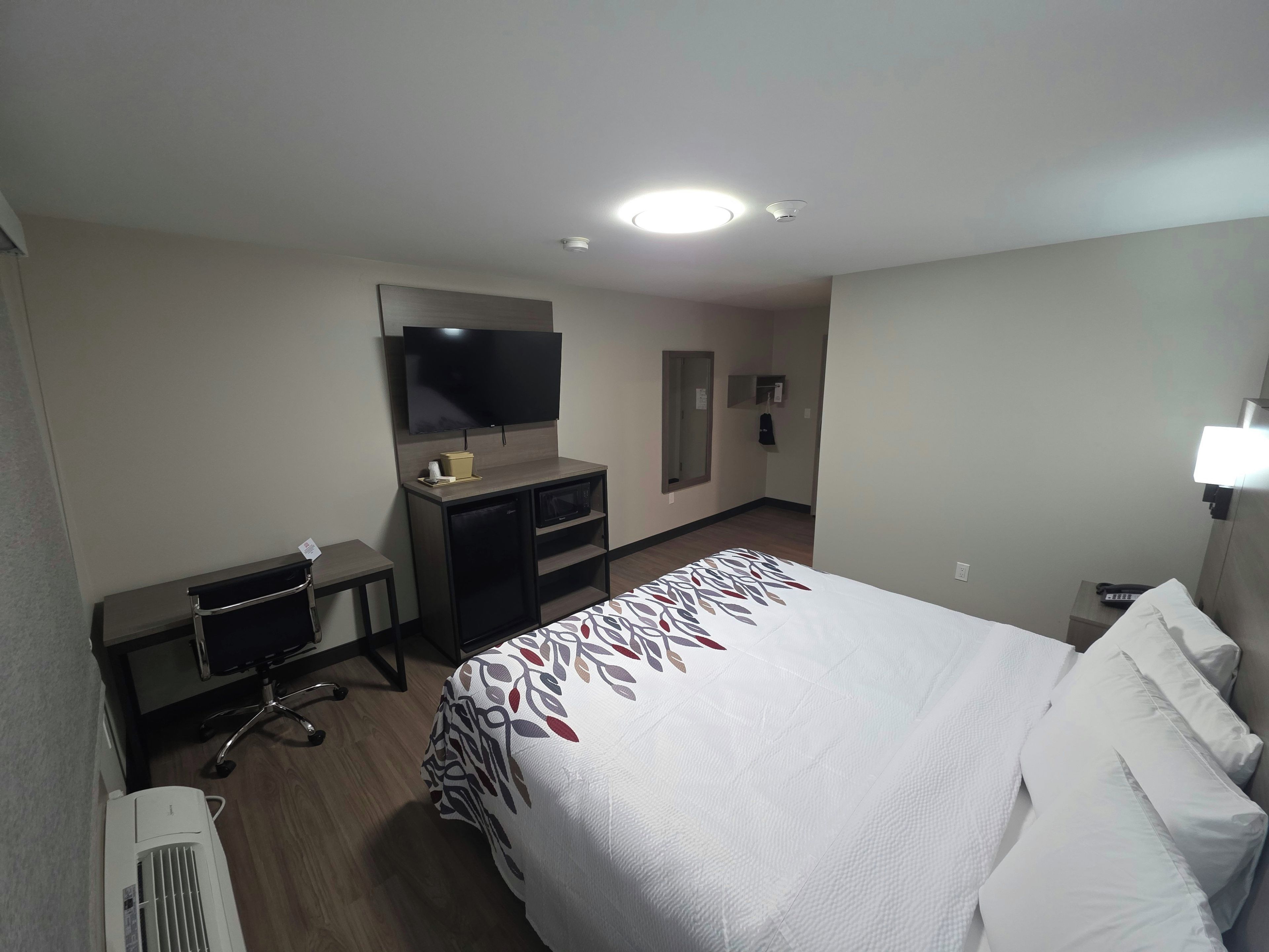 A hotel room with a bed, a desk, a chair, a television, and a mirror.