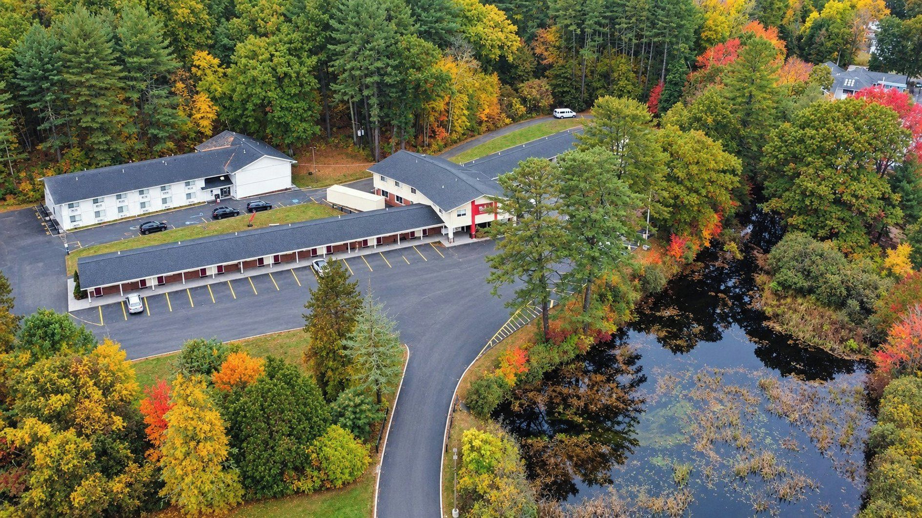 A motel with a parking lot and a road curving around a body of water.