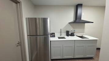A compact kitchen with a stainless steel refrigerator, a black range hood, and a white countertop.