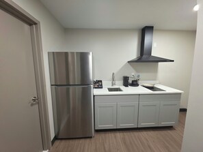 A compact kitchen with a stainless steel refrigerator, a black range hood, and a white countertop. - Red Roof Inn Sutton (Sutton)
