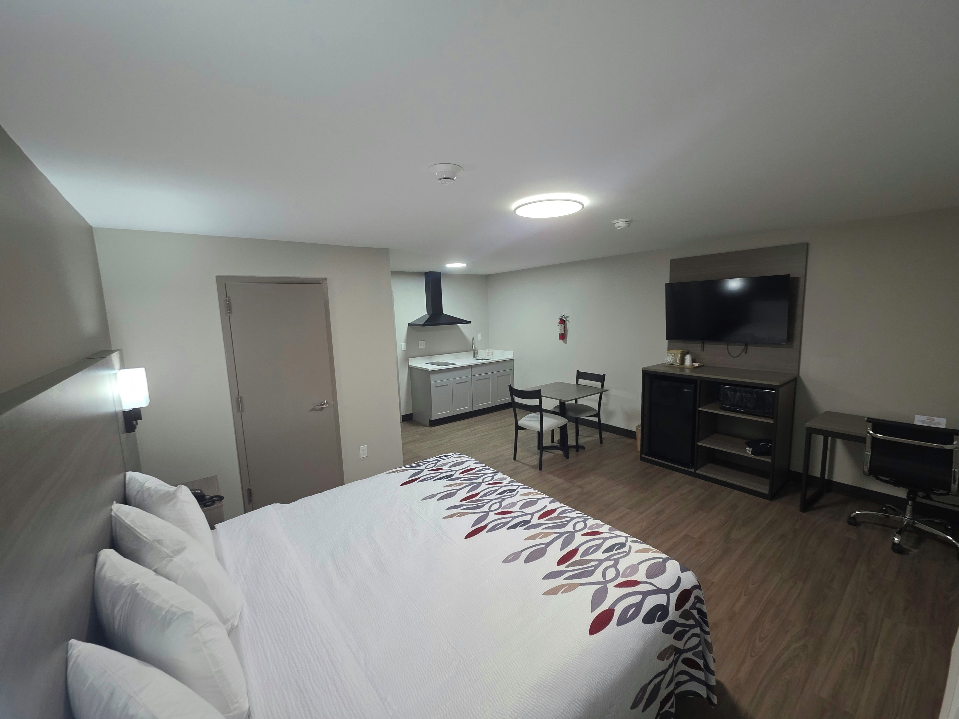 A hotel room with a bed, a desk, a chair, a television, and a kitchenette.