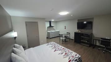 A hotel room with a bed, a desk, a chair, a television, and a kitchenette.