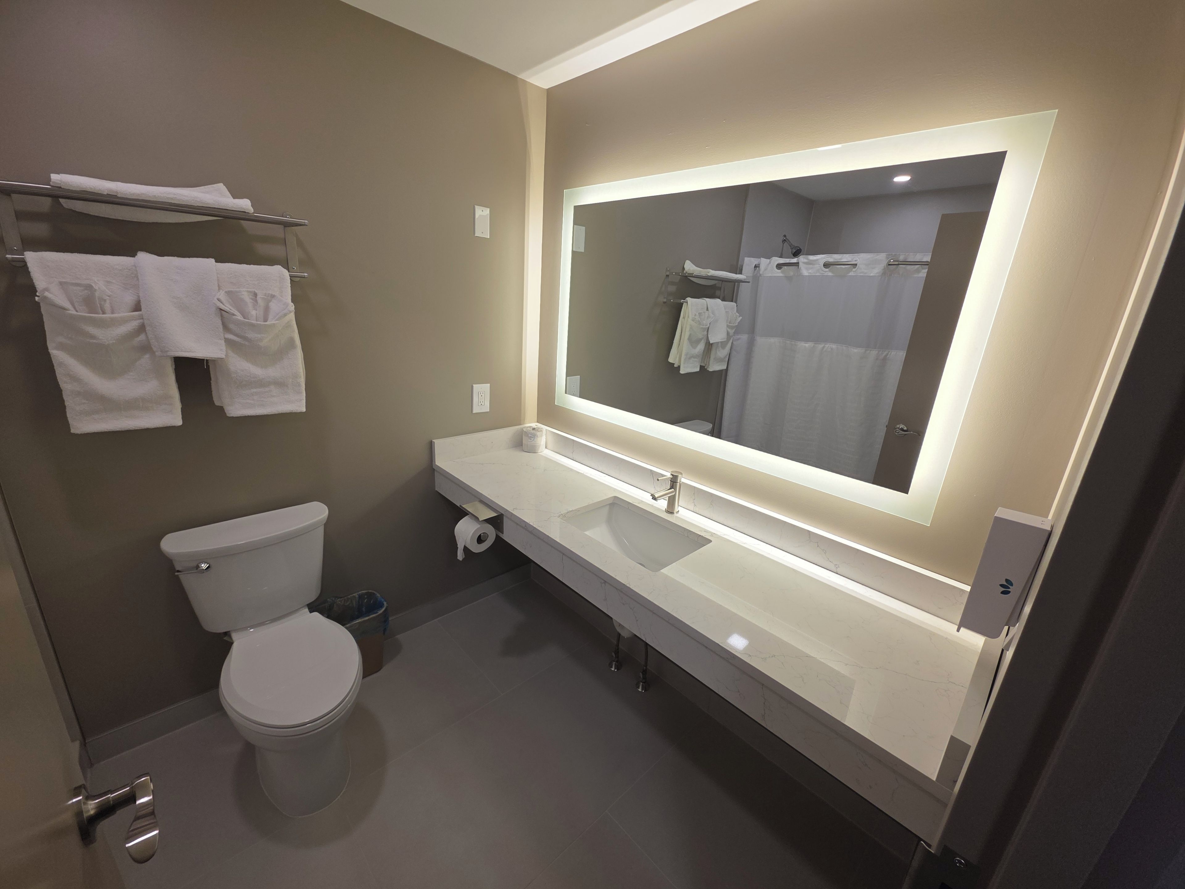A modern bathroom with a toilet, sink, and large mirror.