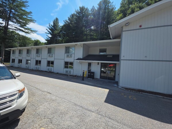 A two-story motel with a row of rooms, a parking lot, and a building with a red awning.