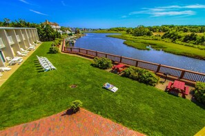 A hotel with a grassy lawn, a river view, and a pool area with lounge chairs. - Riverview Resort (South Yarmouth)