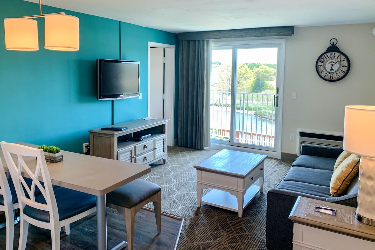 Una sala de estar con televisor, comedor con sillas, sofá, mesa de centro y vista a una piscina a través de puertas correderas.