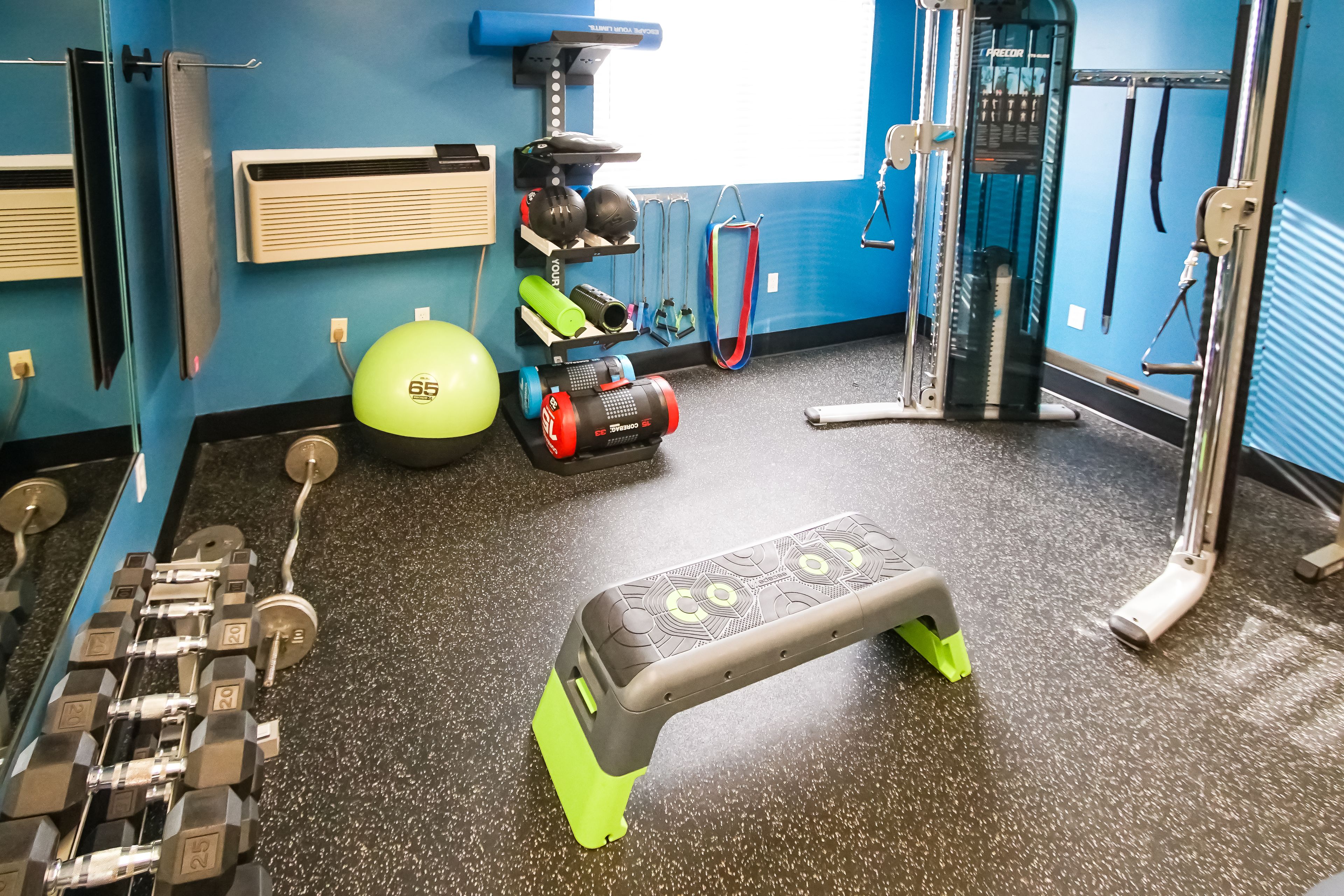 Ginásio com equipamentos de exercício, plataforma elevada e parede com espelhos.