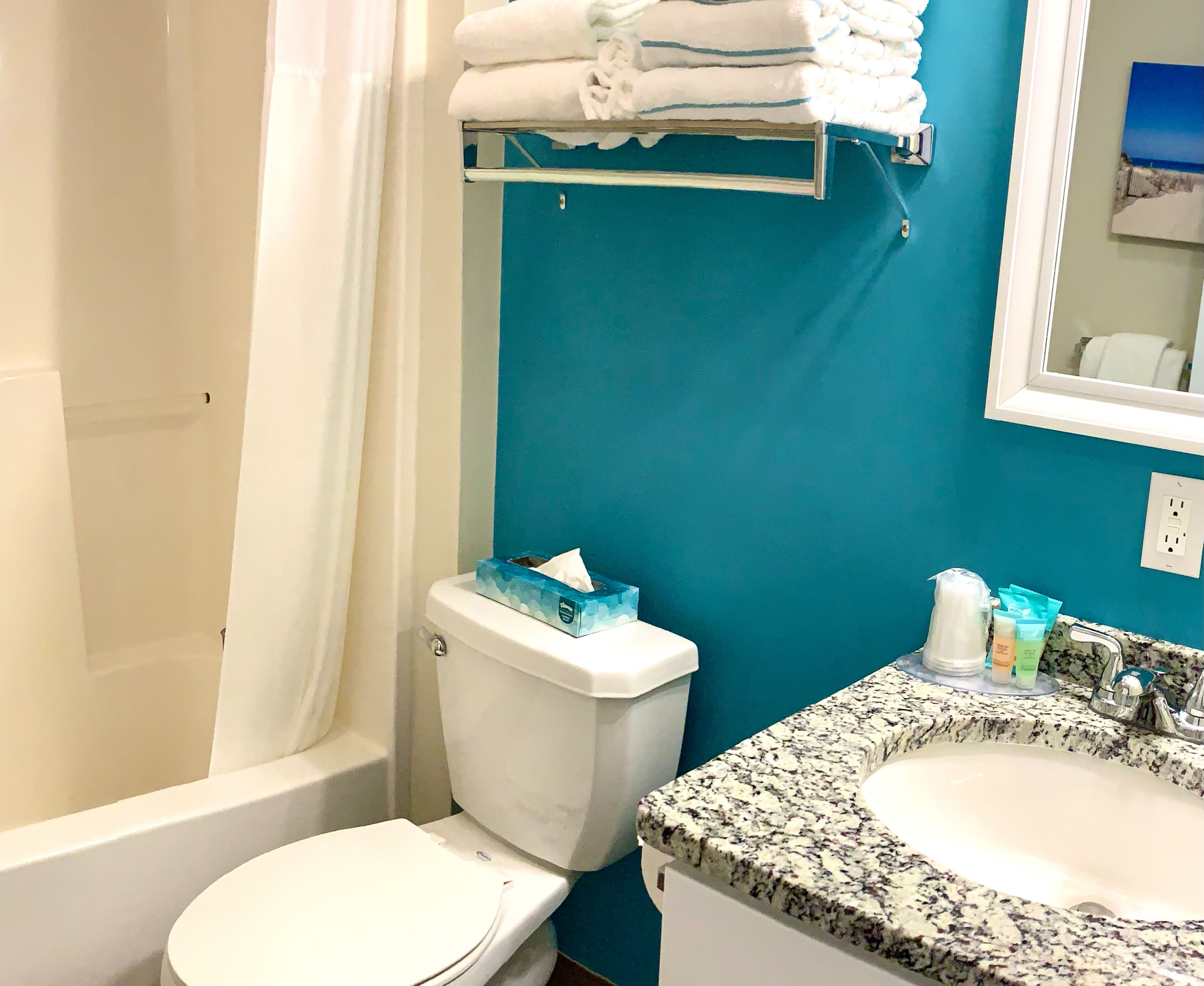 Et badeværelse med et hvidt toilet, en vask med en granitbordplade og et håndklædestativ med foldede håndklæder.