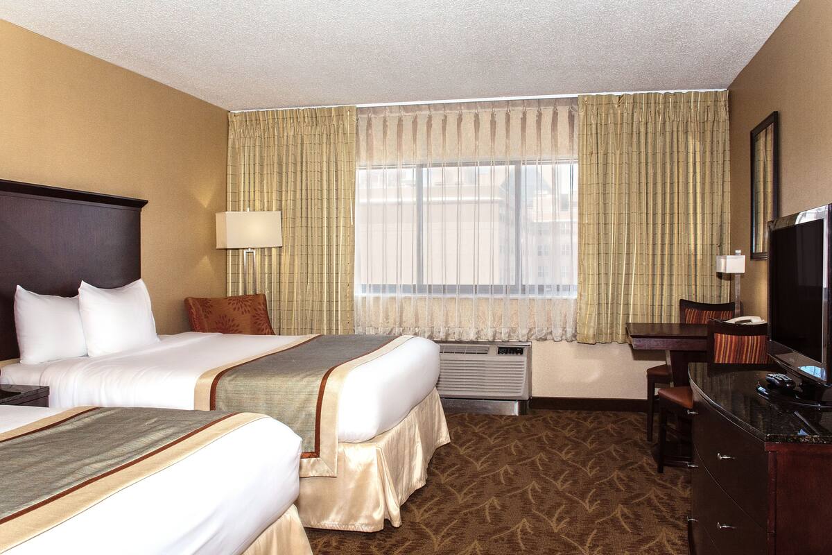 A hotel room with two beds, a desk, a television, and a window with curtains.