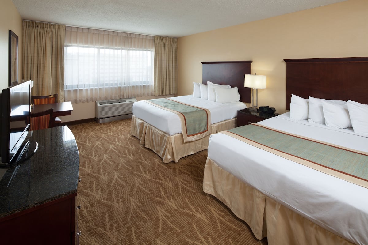 A hotel room with two beds, a desk with a chair, a TV, and a window with curtains.