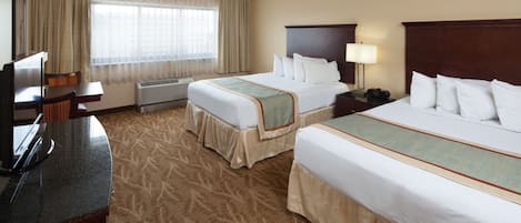 A hotel room with two beds, a desk with a chair, a TV, and a window with curtains.