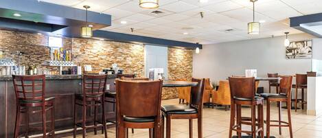 A restaurant with a bar area, wooden chairs, and a stone wall.