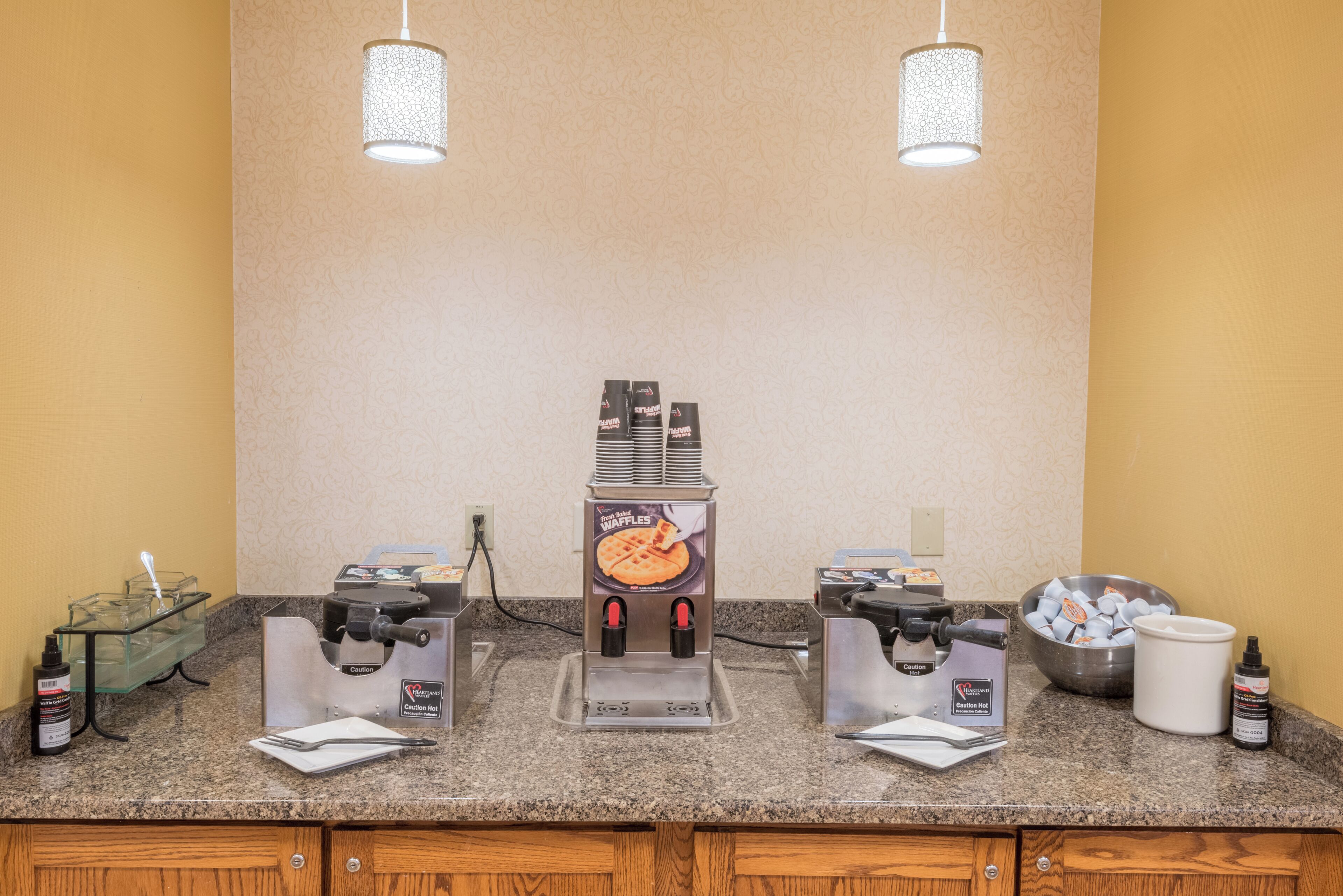 A kitchen area with three waffle makers, a coffee machine, and a bowl of waffle mix.