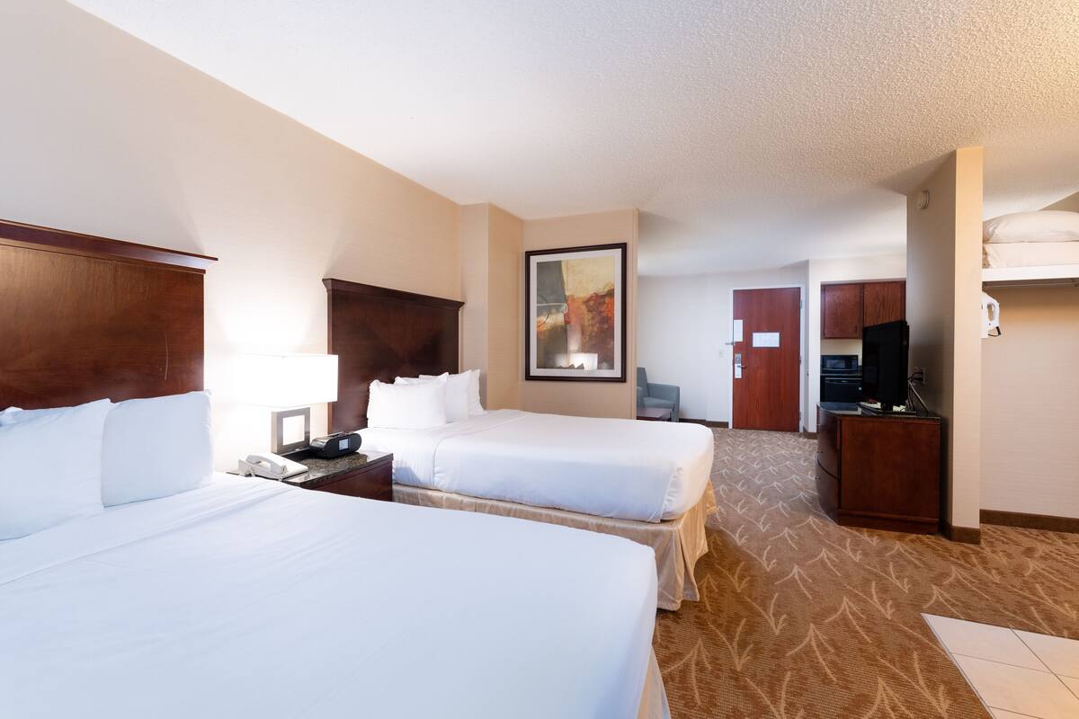 A hotel room with two beds, a desk, a chair, a TV, and a painting on the wall.