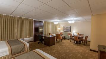 A hotel room with two beds, a desk, a chair, a sofa, and a dining table.