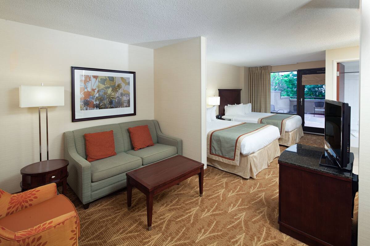 A hotel room with a sofa, a bed, a TV, and a painting on the wall.