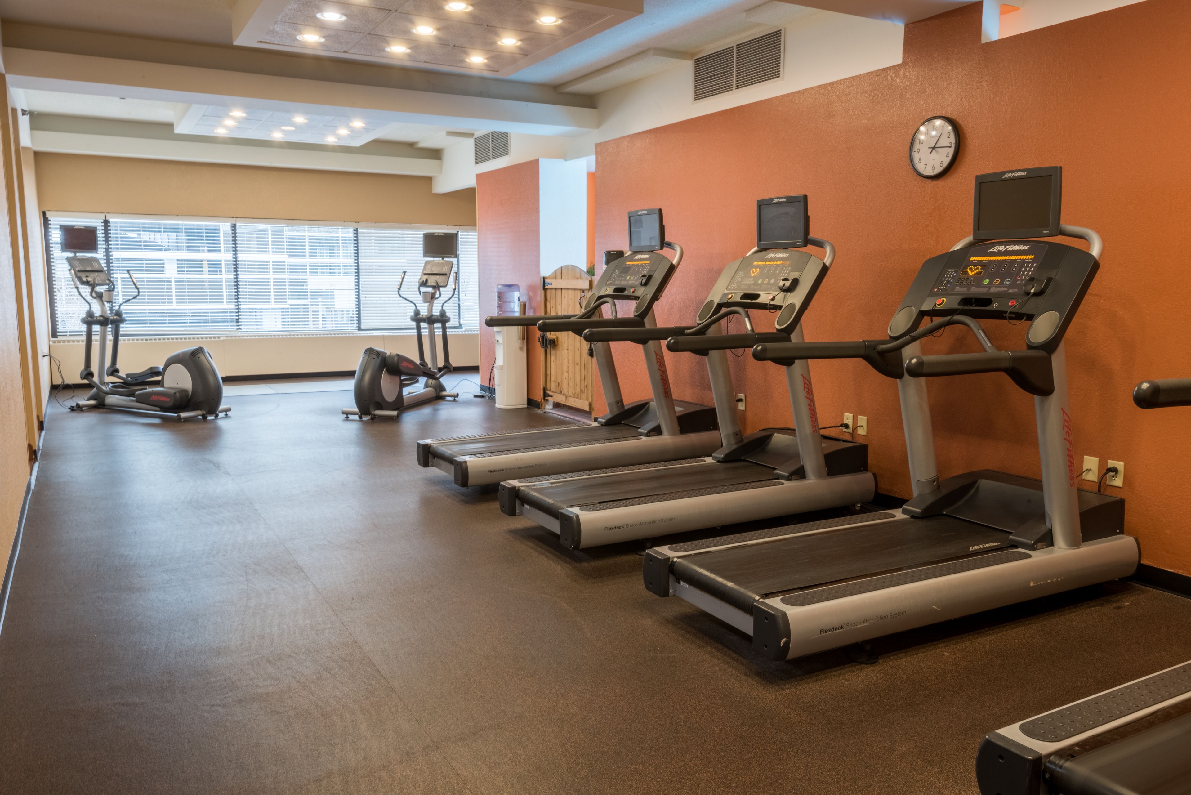 A gym with treadmills, ellipticals, and a wall clock.