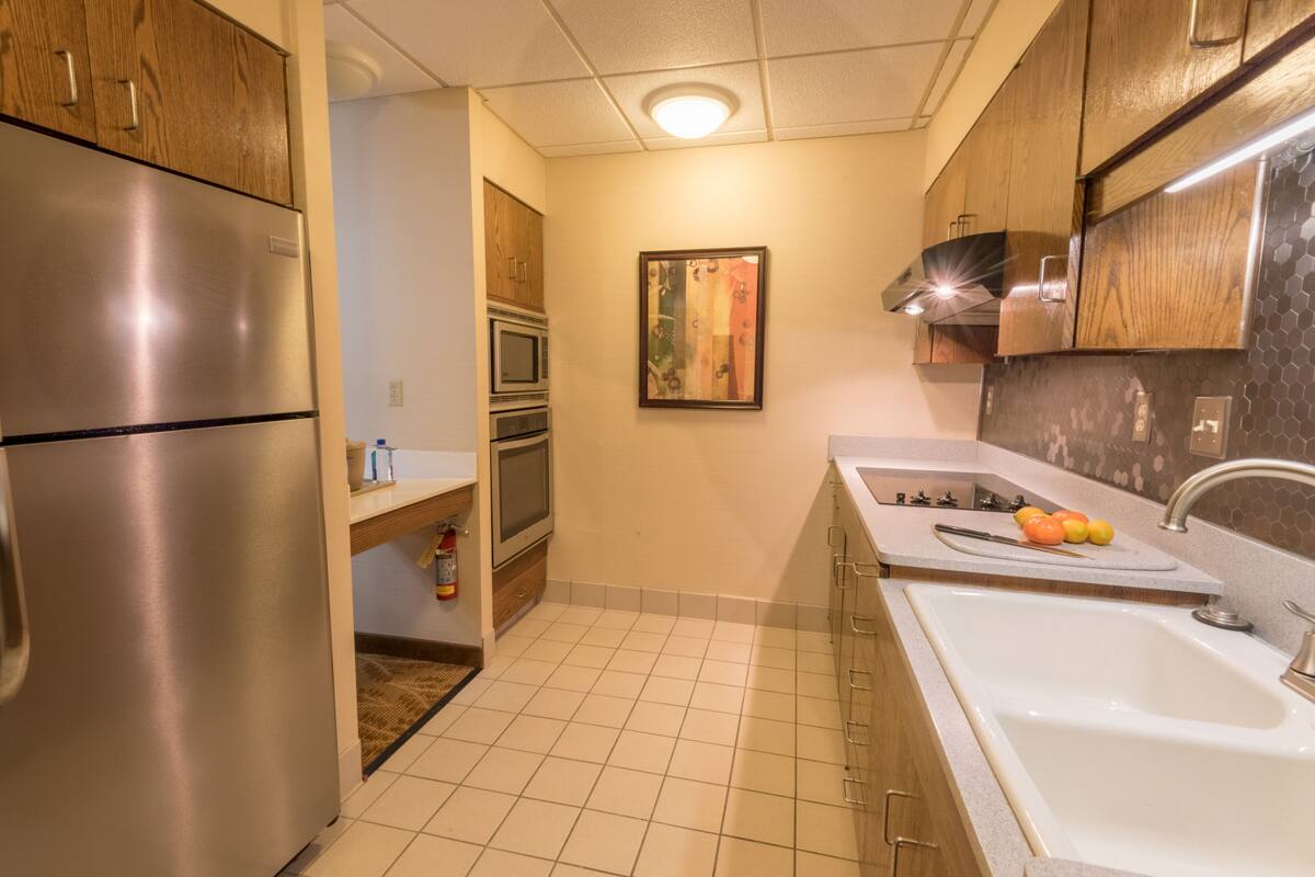 A kitchen with a stainless steel refrigerator, a microwave, a sink, and wooden cabinets.