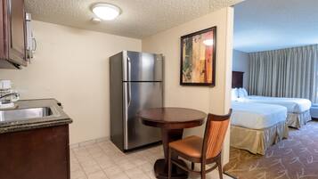 A hotel room with a kitchenette, a bed, a dining table, and a chair.
