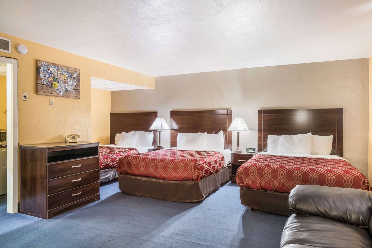 A hotel room with two beds, a dresser, a desk, and a wall map.