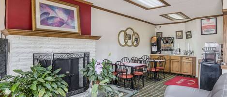 A hotel lobby with a fireplace, dining area, and kitchen.