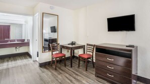 Habitación de hotel con un escritorio de madera, dos sillas rojas, un televisor montado en la pared, un espejo y un armario.