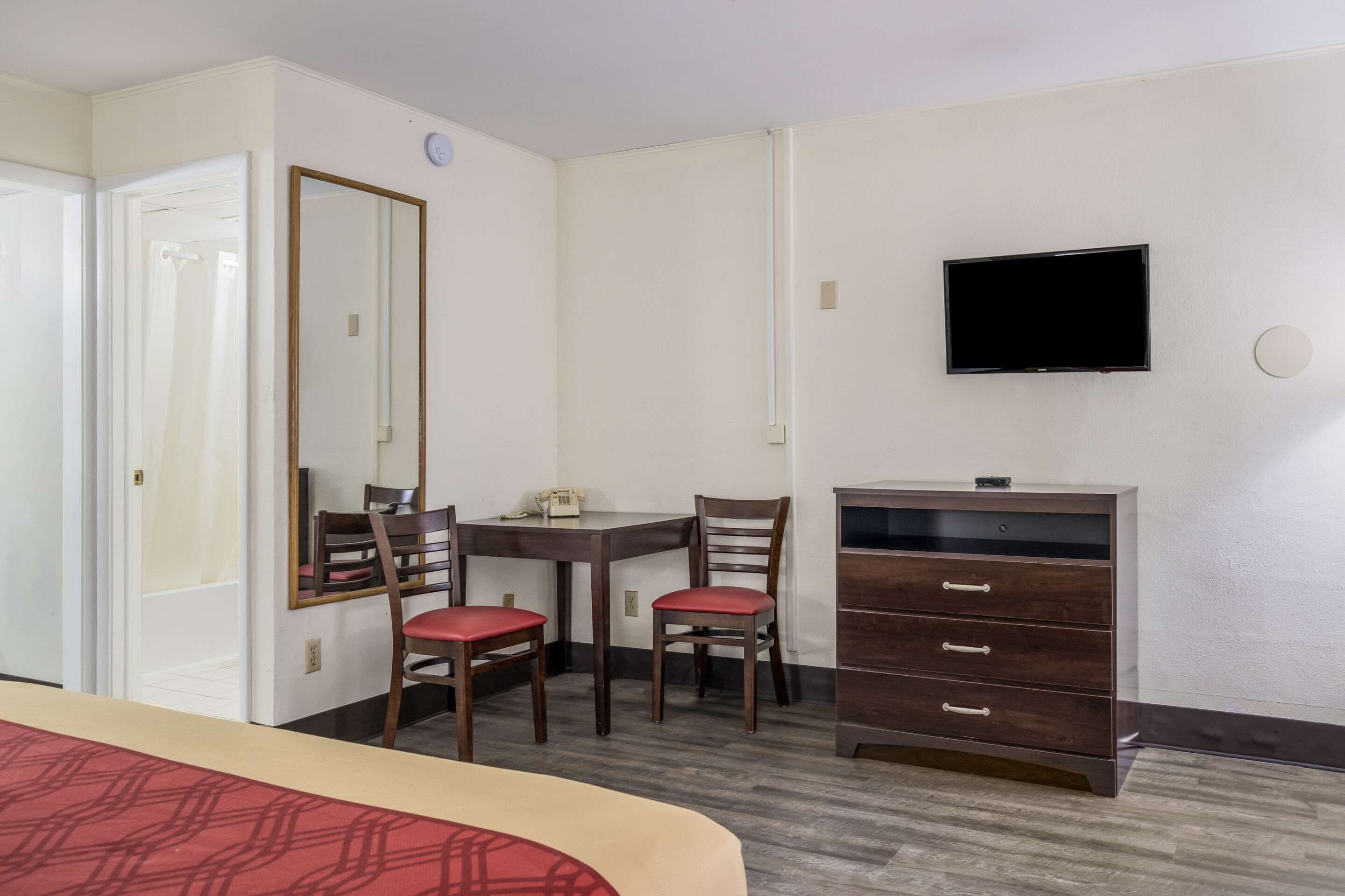 A hotel room with a bed, a desk with two chairs, a dresser, a television, and a mirror.